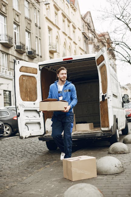 Two removal personnel from Man with Van South Woodford are engaged in loading a van for house relocation on South Woodford's High Road. One person, wearing a white shirt and black cap, is carefully li